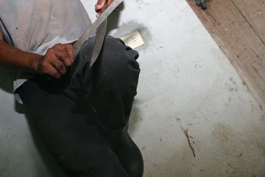 A young man sharpens his machete against a rustic wall in Costa Rica.