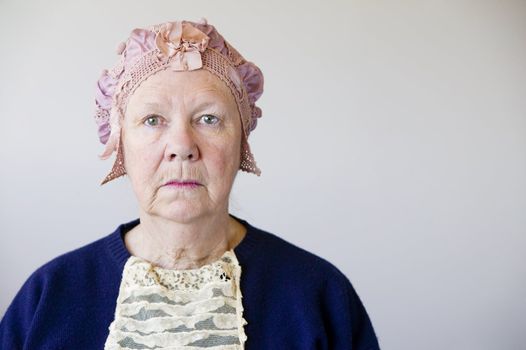 Dour senior woman in the studio wearing a vintage hat and lace.