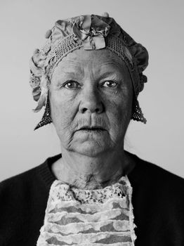 Dour senior woman in the studio wearing a vintage hat and lace.