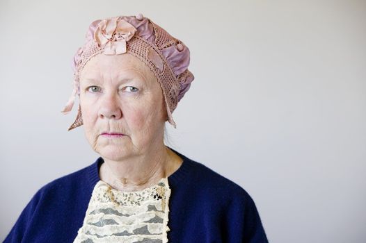 Dour senior woman in the studio wearing a vintage hat and lace.