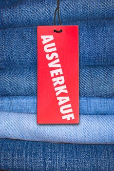 Red German Sale Sign With Stack of Blue Jeans in Background