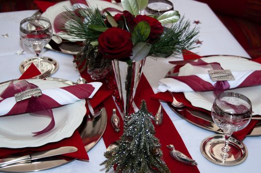 Christmas table with red decoration, napkins, roses, silver, christmas tree and candles