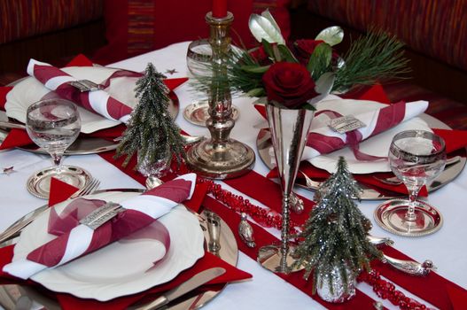 Christmas table with red decoration, napkins, roses, silver, christmas tree and candles