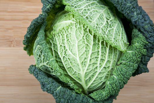 Head of curly green leaf cabbage on cutting board.  Angle of view from directly above.
