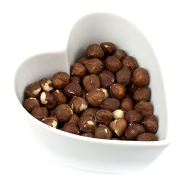Brown roasted hazelnuts in a heart shaped bowl isolated on white