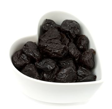 Prunes in a heart shaped bowl isolated on white background