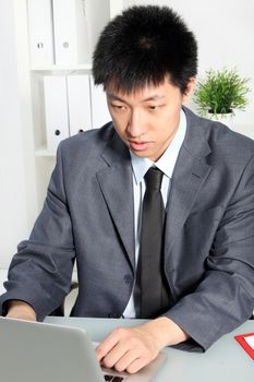 Young professional Asian man focusing on his work on computer, at his desk