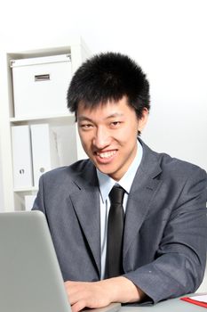Enthusiastic young Asian businessman working on computer, at his desk