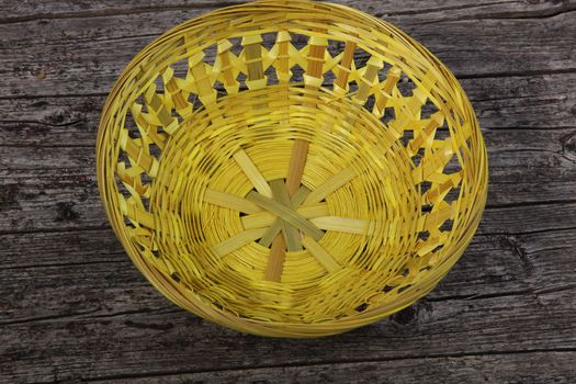 High angle view of the inside of a shallow empty woven cane basket on a rustic weathered cracked wooden plank background