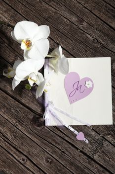 Pretty hand made Valentine card with a purple heart and fresh white flowers on an old cracked weathered wooden background