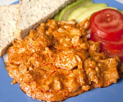 Serving of chicken tikka on a blue plate with vegetables and bread