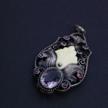Vintage style silver and gemstone pendant with a large faceted amethyst in the foreground lying on a dark studio background with copyspace