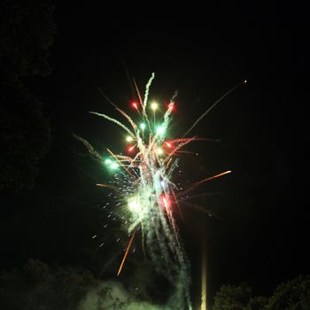 Colorful festive fireworks display lighting up the dark night sky with bursts of fiery red and green