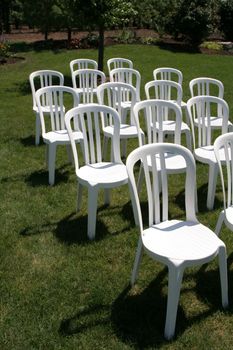 A bunch of whit plastic chairs organized on green grass.