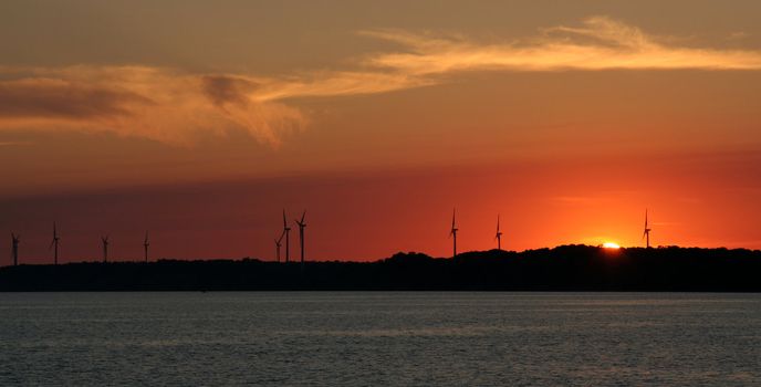 The sun setting just over the horizon with wind turbines in the background.