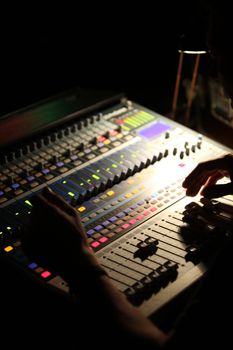 Person mixing music at a control console in shadowed darkness during a recording or performance