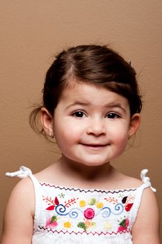 Cute happy smiling young toddler girl in white shirt on brown.