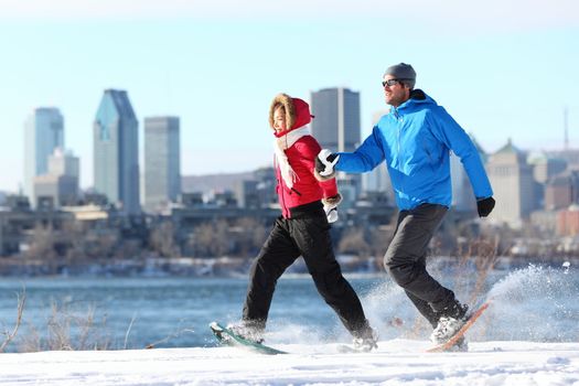 Happy couple snowshoeing running in montreal with cityscape skyline and river st. Lawrence in background. Healthy lifestyle photo from Montreal, Quebec, Canada.