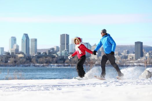 Winter fun couple on snowshoes running with montreal cityscape skyline and river st. Lawrence in background. Healthy lifestyle photo from Montreal, Quebec, Canada.