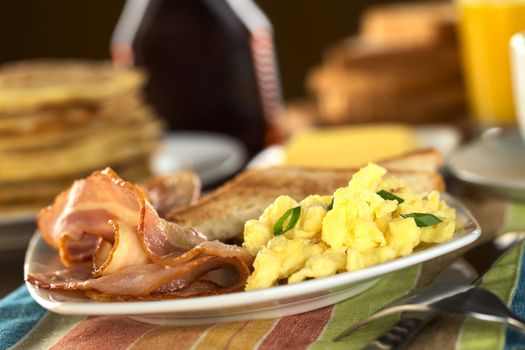 Fried bacon and scrambled eggs with toast bread, pancakes and orange juice in the back (Selective Focus, Focus one third into the meal)