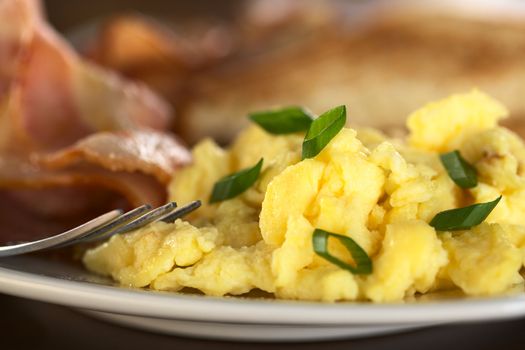 Scrambled eggs and green onions with fried bacon and toast bread in the back (Selective Focus, Focus on the green onion on the top and the egg in the same plane) 