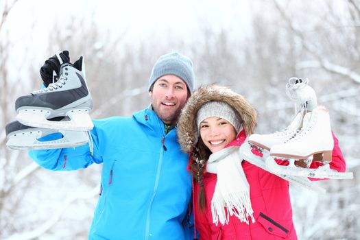 Ice skating winter couple smiling happy and excited showing ice skates outdoors in snow. Beautiful young multi-racial couple healthy lifestyle concept.