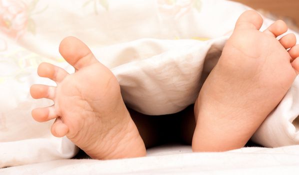 The tiny feet of a newborn baby under a blanket