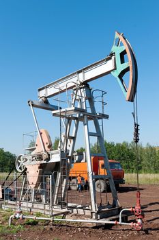 Oil pumping unit with  car service in the background