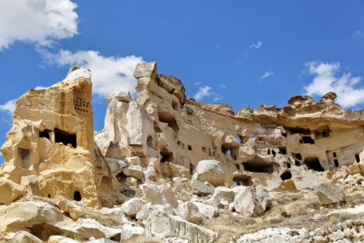 Landscape on outskirts of Goeme, Cappadocia, of ancient township built into limestone caves showing exterior architecture, flying high is a Turkish flag, blue cloudy sky with negative area and crop margins