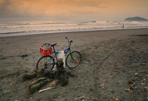A bike parked on the beach belongs to a fisherman far in the distance.