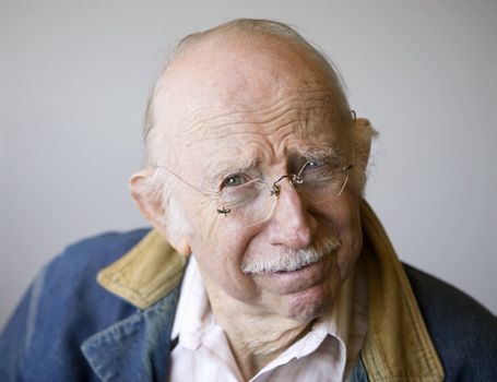 Portrait of a senior citizen wearing glasses and a jean jacket in a studio.