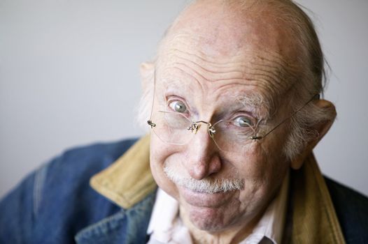 Portrait of a senior citizen wearing glasses and a jean jacket in a studio.