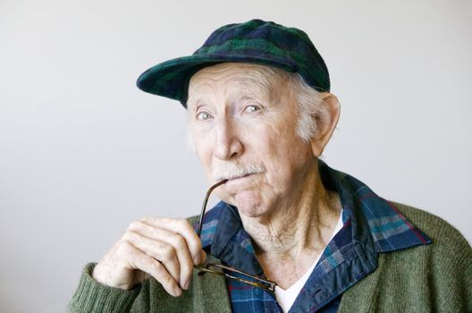 Portrait of a thoughtful senior citizen with glasses wearing a hat.