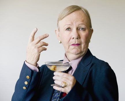 Dramatic senior woman in a man's suit holding a Martini.