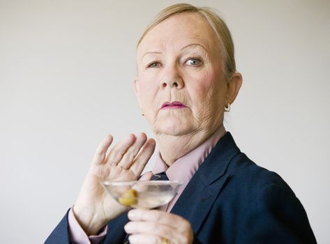 Dramatic senior woman in a man's suit holding a Martini.