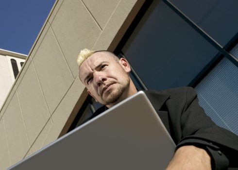 Businessman with a punk haircut looks over the top of his laptop computer in an office complex.