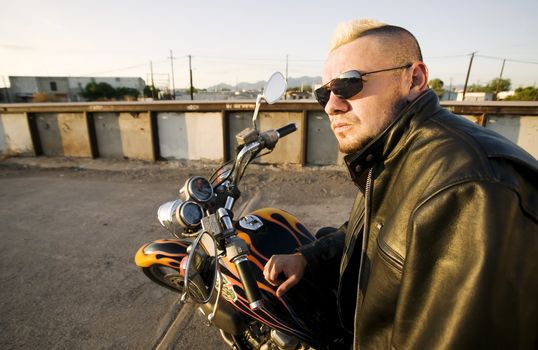 Man with a punk haircut in a leather jacket sitting on his motorcycle.