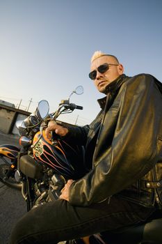 Man with a punk haircut in a leather jacket sitting on his motorcycle.