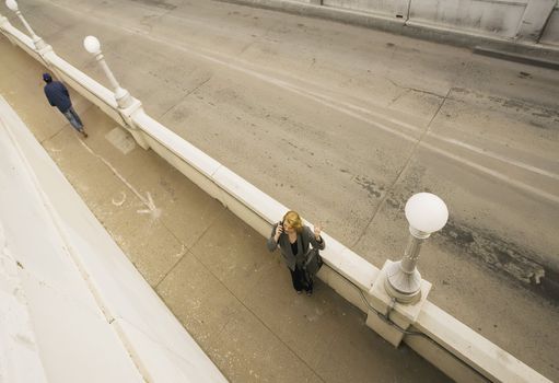 Wide shot from above of  woman on her cell phone next to an empty road.