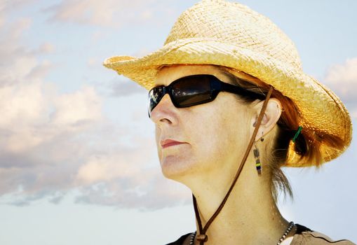 Woman in bright sun wearing a cowboy hat looks off to the side.