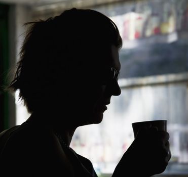 A woman  in silhouette drinks a morning cup of coffe.