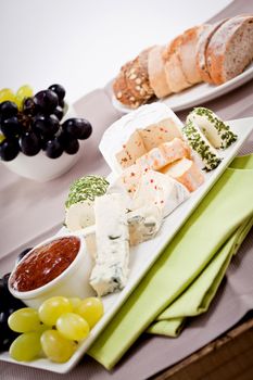different cheese types on plate with grapes and red wine on wooden table