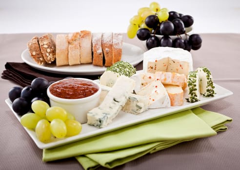 different cheese types on plate with grapes and red wine on wooden table