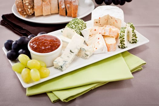 different cheese types on plate with grapes and red wine on wooden table