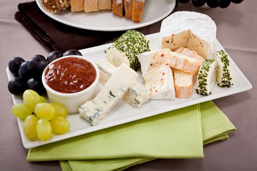 different cheese types on plate with grapes and red wine on wooden table
