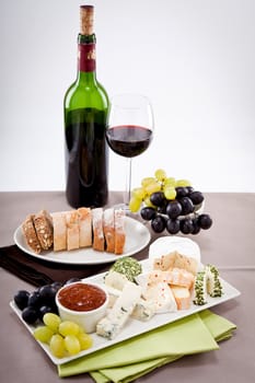 different cheese types on plate with grapes and red wine on wooden table