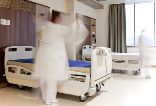 Blurred figure of staff in medical uniform fixing bed in modern hospital room