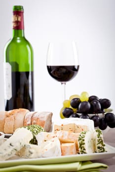 different cheese types on plate with grapes and red wine on wooden table
