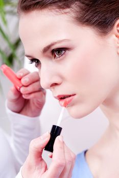 brunette attractive woman portrait applying lipstick lipgloss in beauty salon
