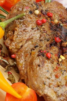 Roasted Beef with Spices, Peppercorns and Herbs closeup on Wooden Board with Vegetables